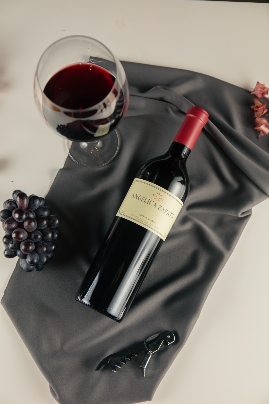 Garrafa de vinho tinto, taça, uvas e saca-rolhas sobre uma mesa